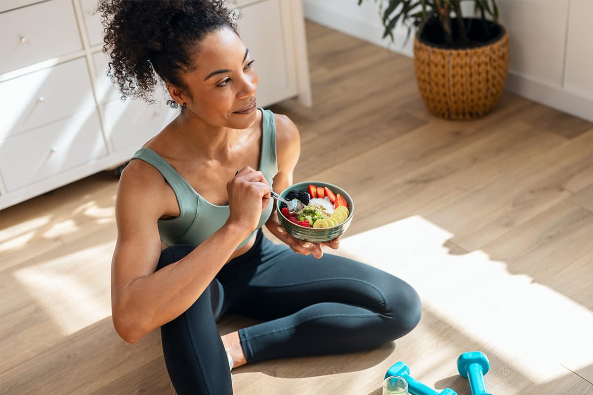 Active woman enjoying a colorful fruit and yogurt bowl post-workout with dumbbells nearby